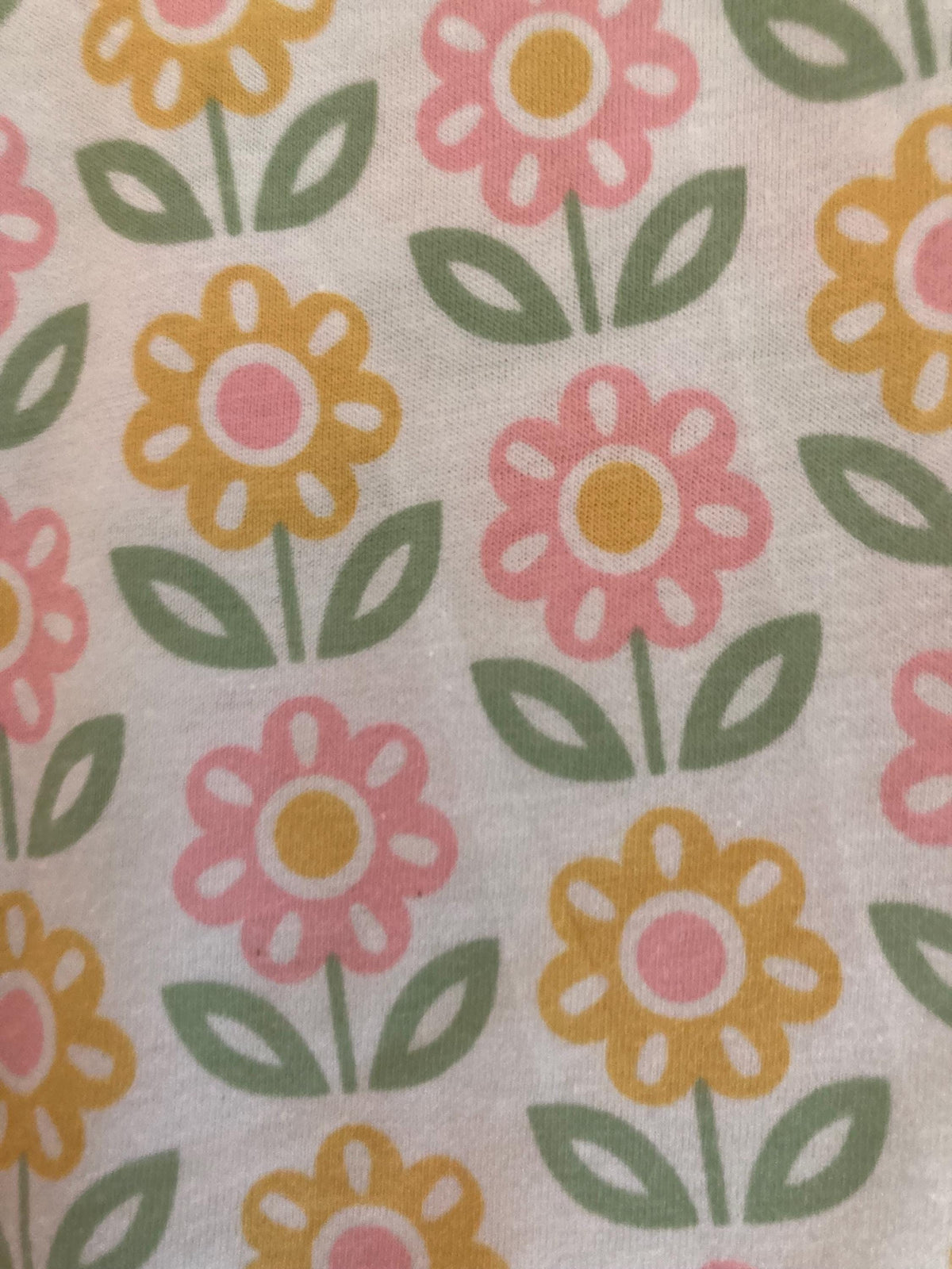 May include: Close-up of a white fabric with a repeating floral pattern. The flowers alternate between pink and yellow, each with a pink center. Green leaves and stems complete the design. The overall aesthetic is cheerful and reminiscent of spring.