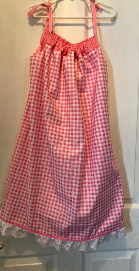 May include: A pink and white gingham dress with a white lace trim at the hem. The dress has pink straps and a gathered neckline. It is hanging on a white hanger.